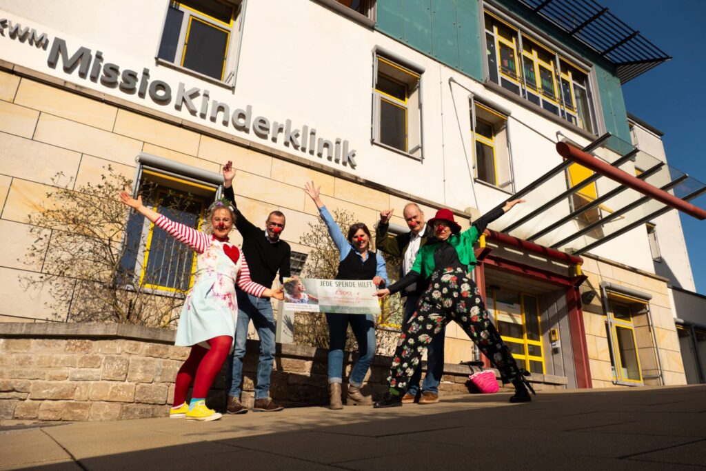 Gruppe vor Missio Kinderklinik mit Clownskostümen fröhlich