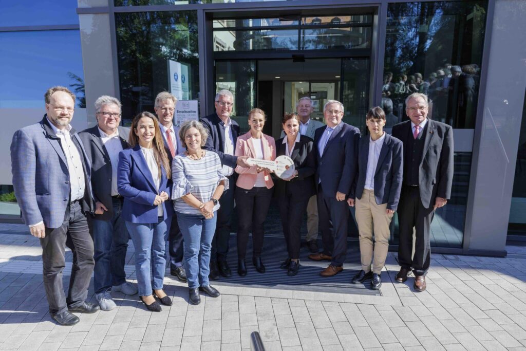 Gruppe von Menschen bei einer Schlüsselübergabe vor Gebäude.