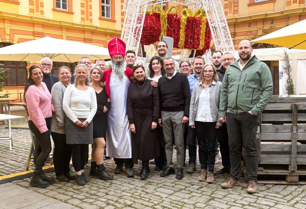 Gruppe posiert vor weihnachtlichen Dekorationen auf gepflastertem Platz.