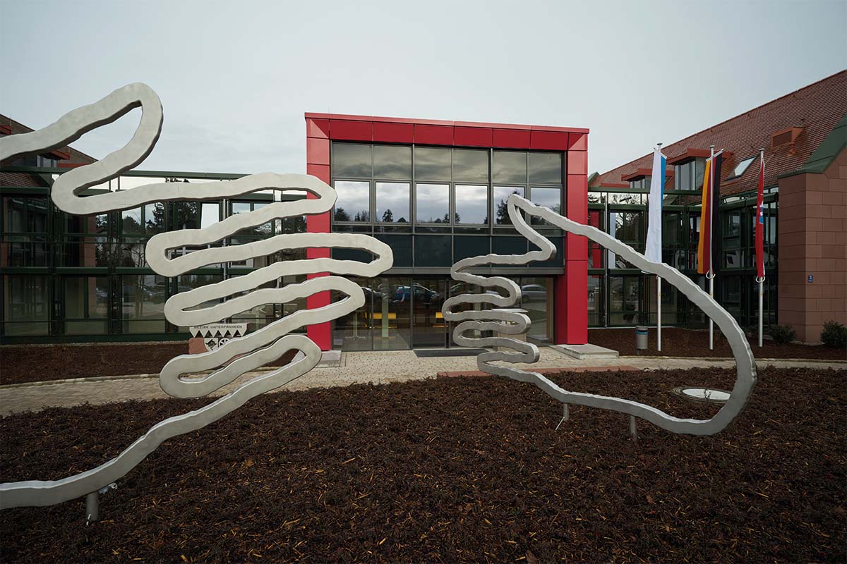 Moderne Glasfassade mit Skulpturen und Fahnen.