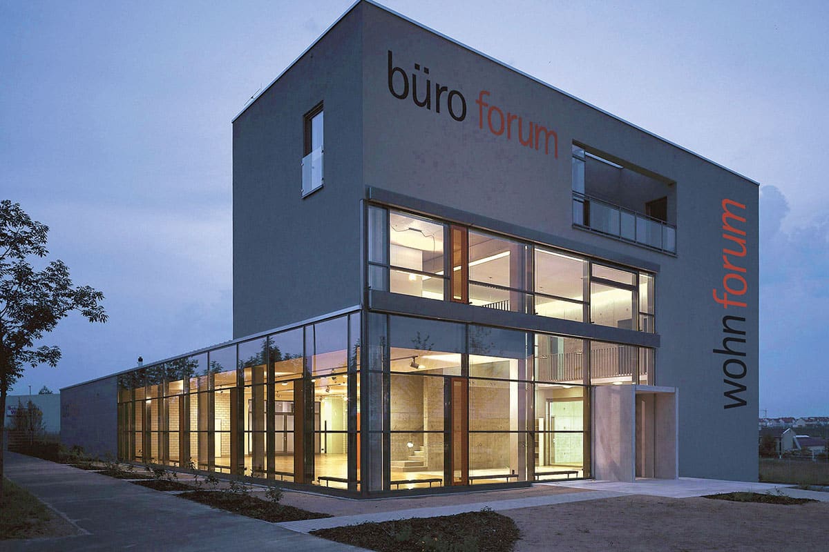 Modernes Bürogebäude bei Abenddämmerung, beleuchtete Fenster.