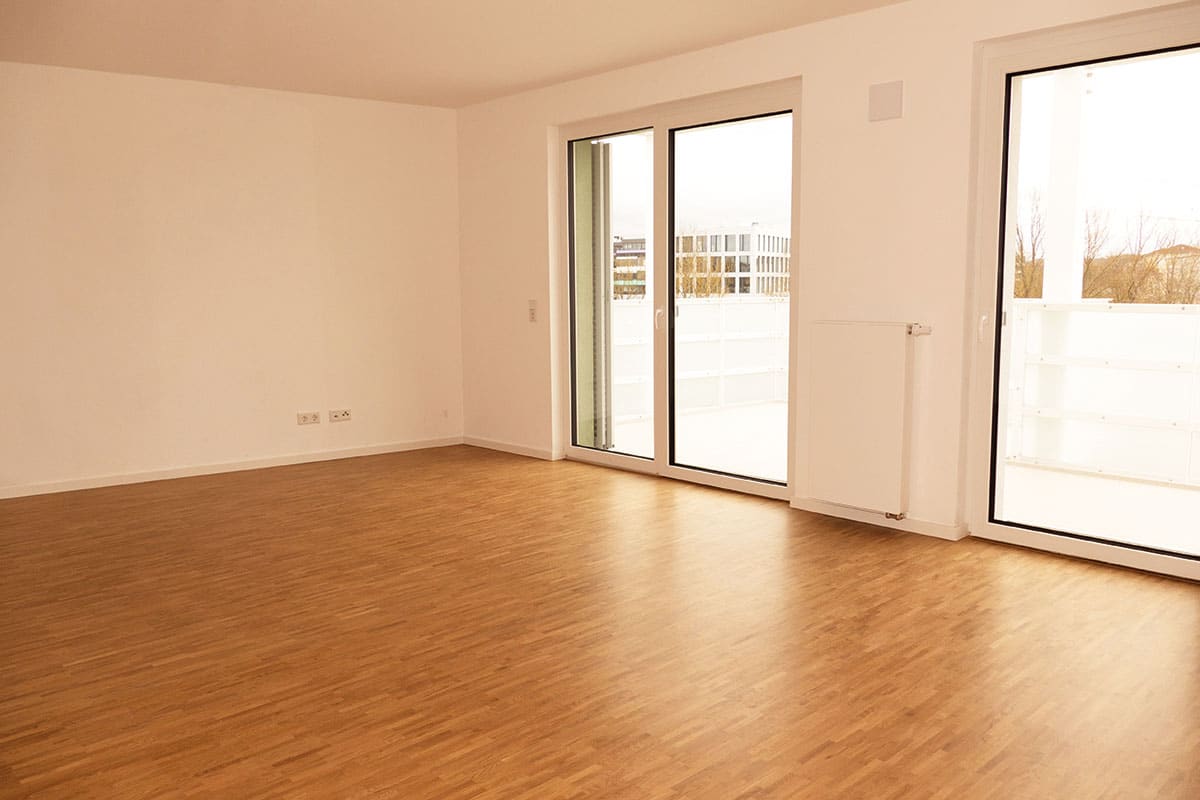 Leerer Raum mit Parkett und großen Fenstern.