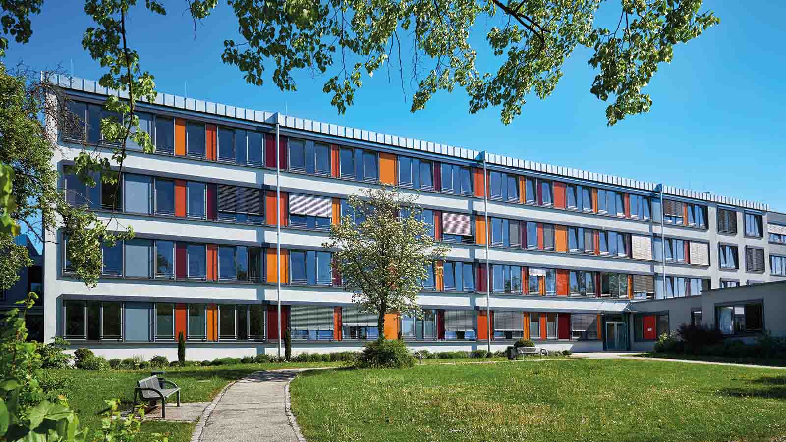 Schulgebäude mit bunten Fenstern und grünem Garten.