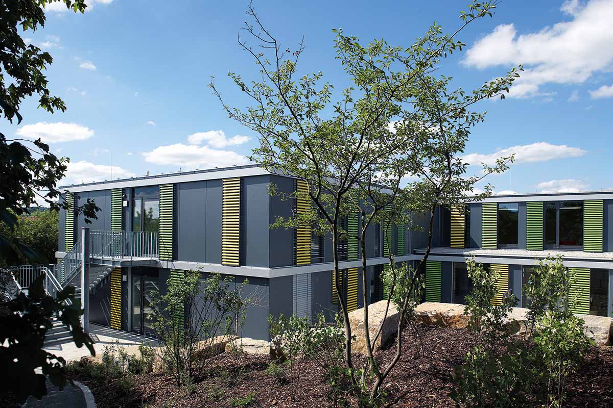 Modernes zweistöckiges Gebäude mit grüner Umgebung, blauer Himmel.