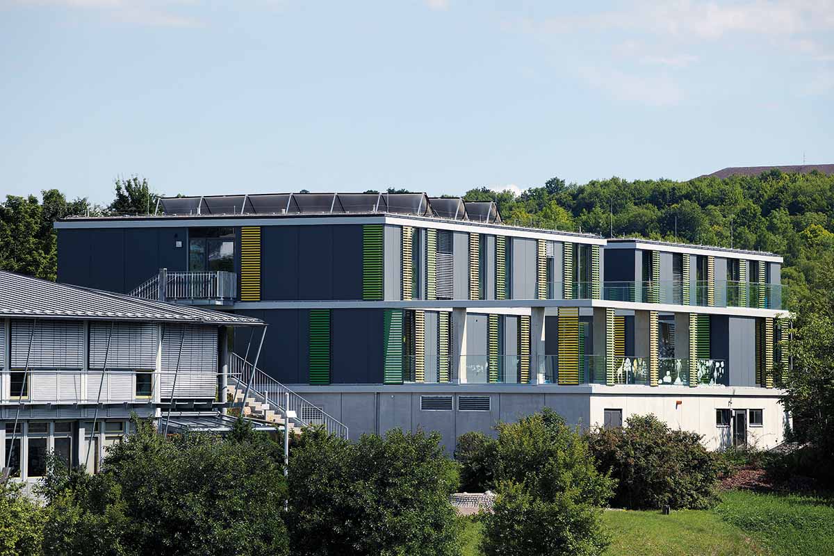 Modernes Gebäude mit bunten Fassaden vor bewaldetem Hintergrund.