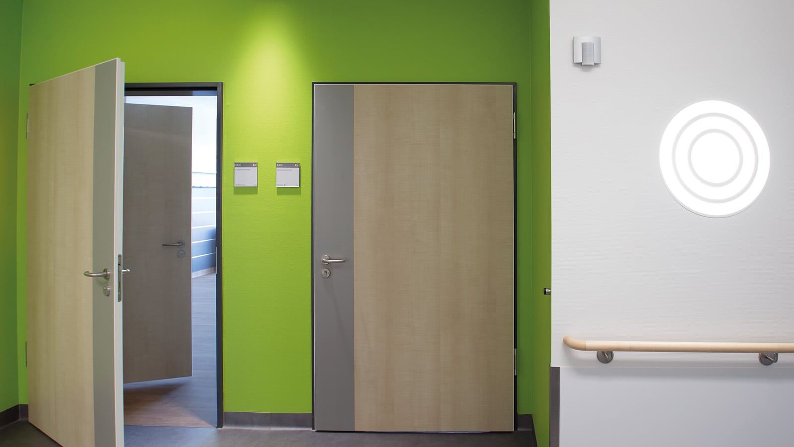 Grüner Flur mit offenen Türen und Wandlicht.