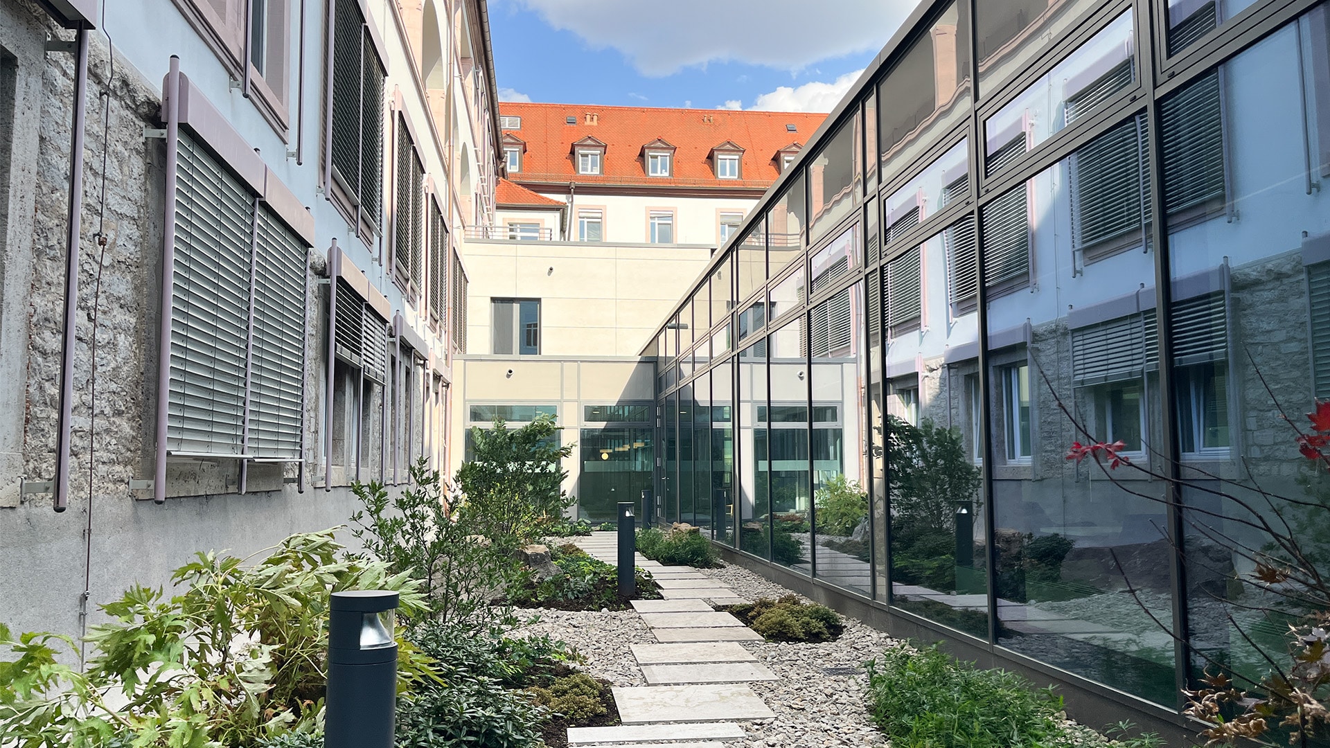 Innenhof mit Glasfassade und Pflanzen, blauem Himmel