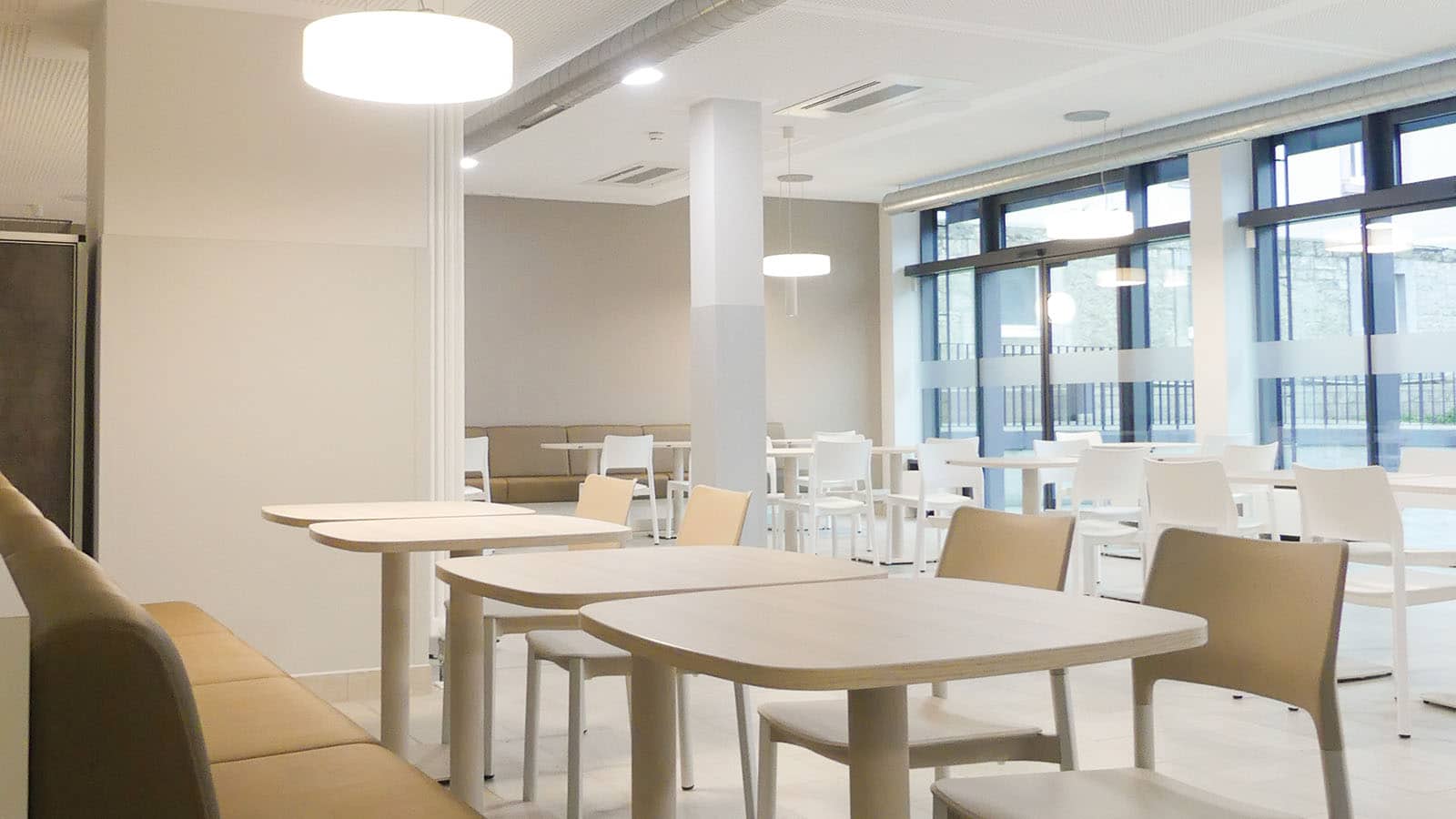 Moderne, lichtdurchflutete Kantine mit weißen Tischen.