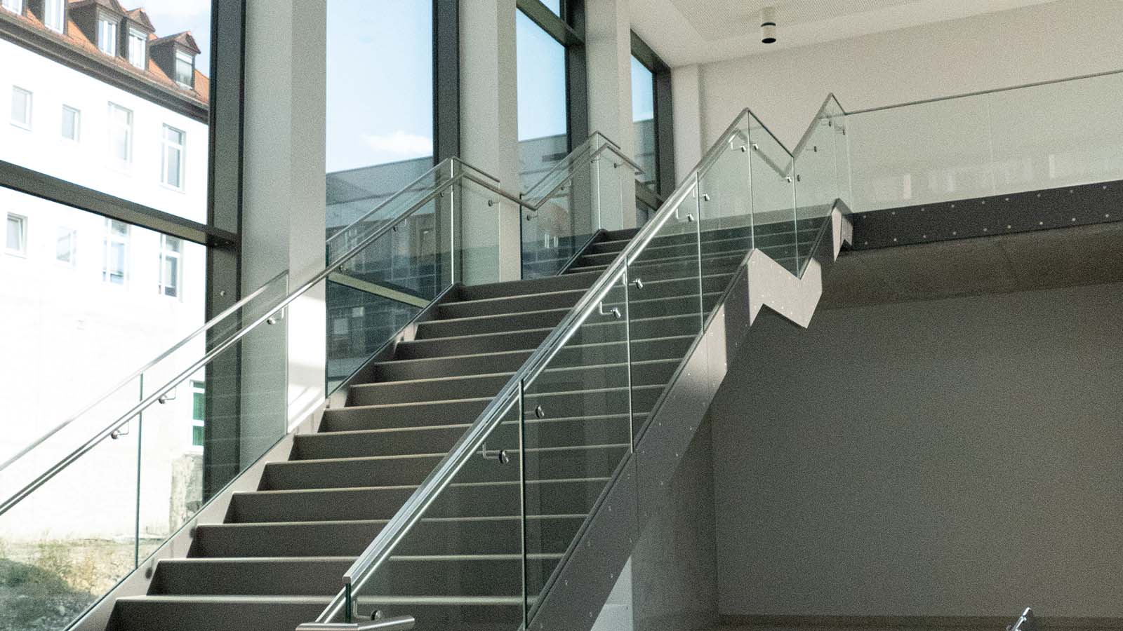 Moderne Treppe mit Glasgeländer in Gebäudeinnerem.