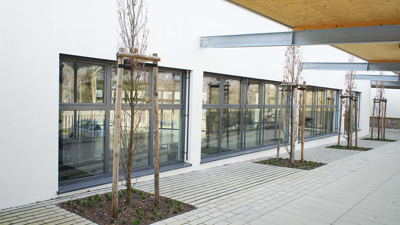 Moderne Fassade mit großen Fenstern und jungen Bäumen.