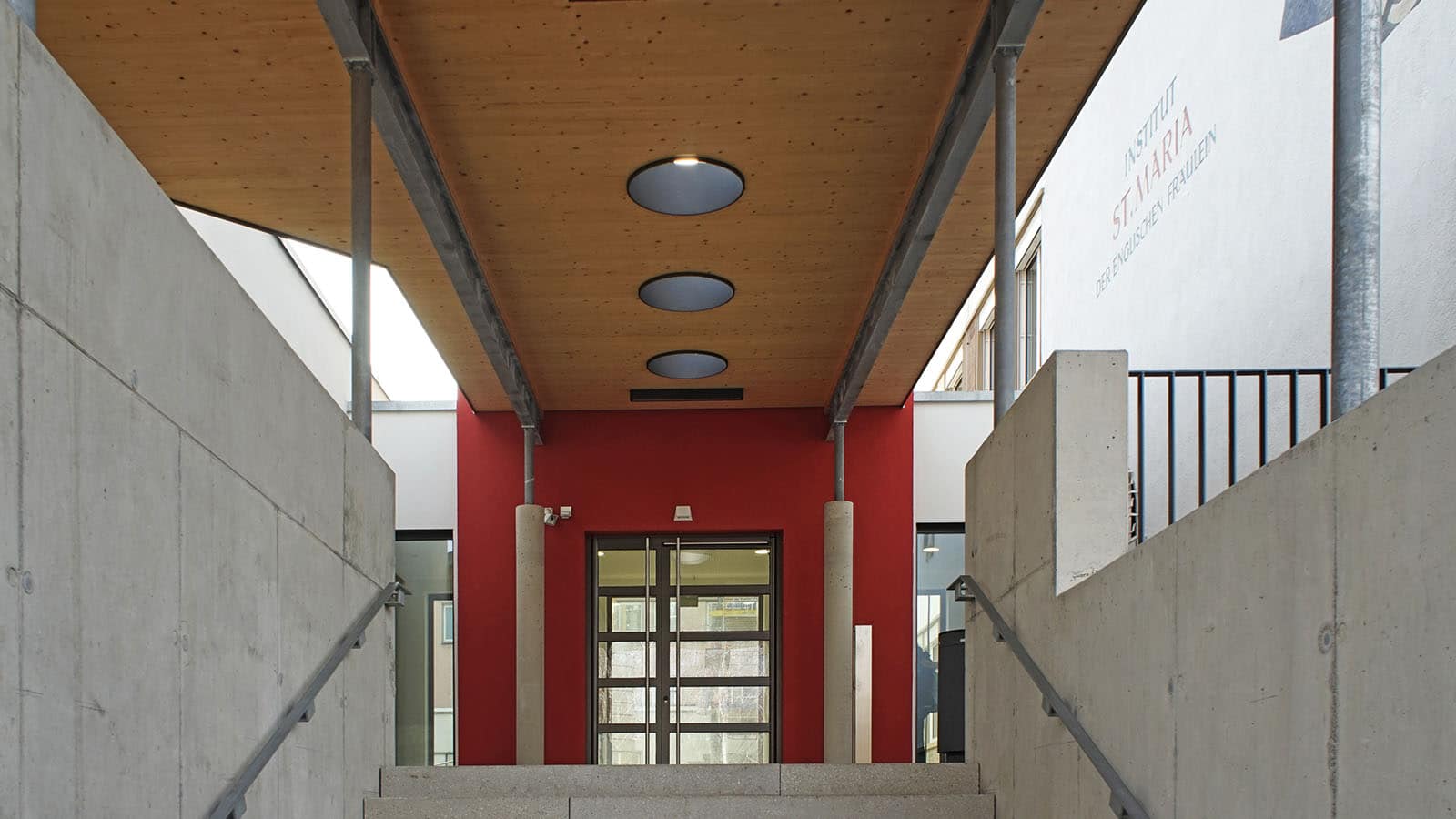 Eingang mit roter Fassade und Zementwänden