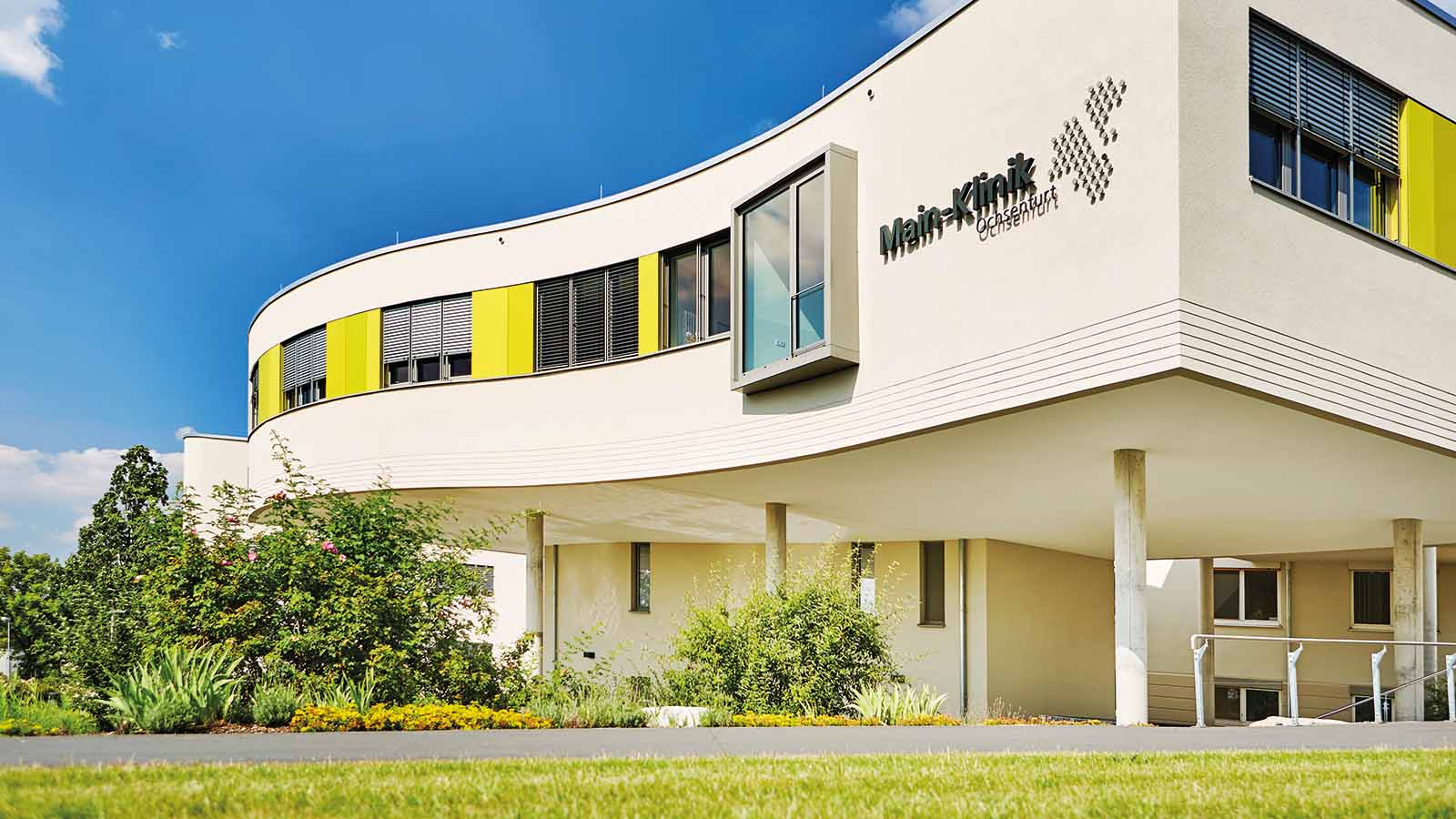 Moderne Klinikgebäude mit Garten und klarem Himmel.