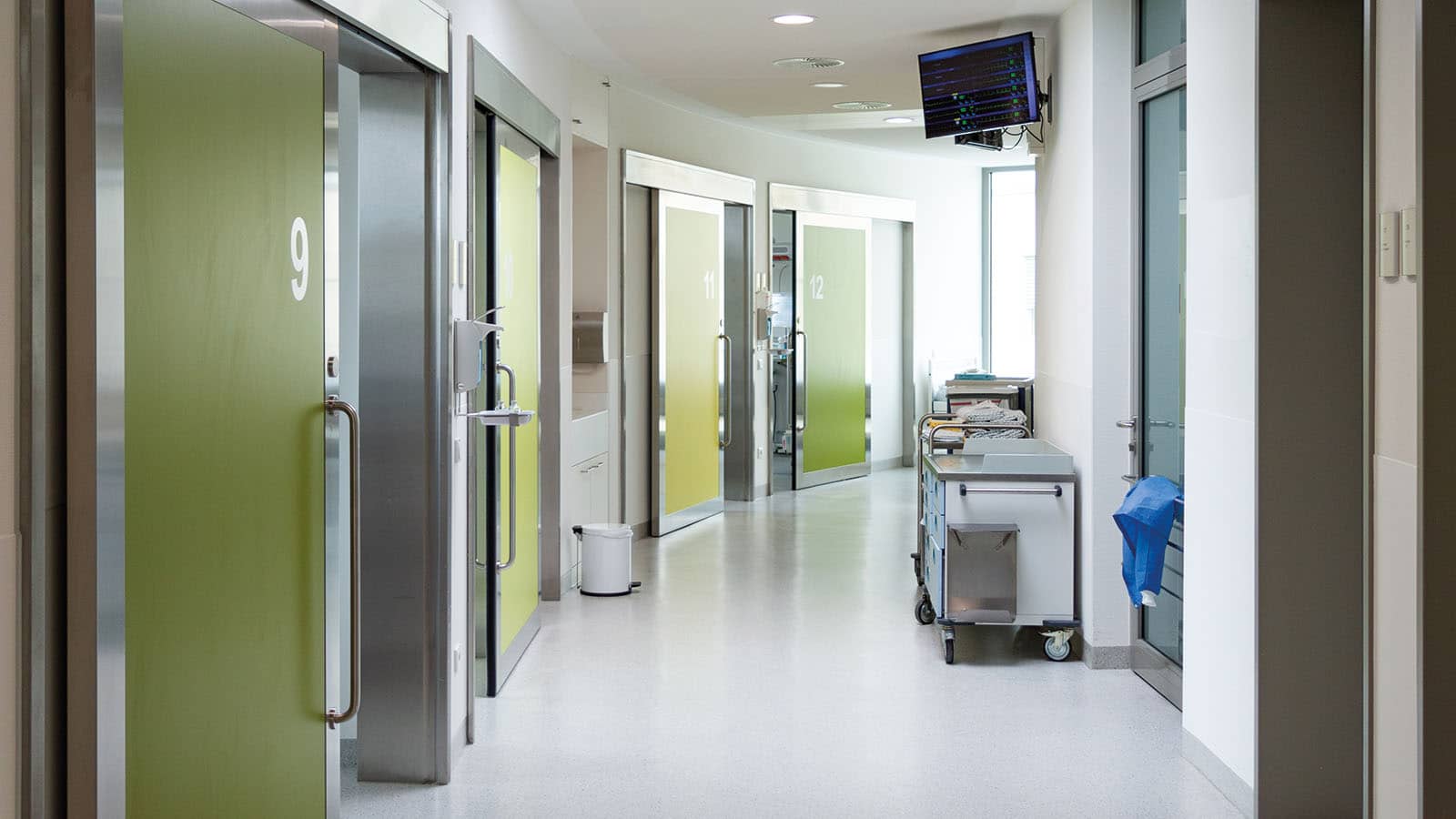 Krankenhausflur mit nummerierten Türen und Geräten.