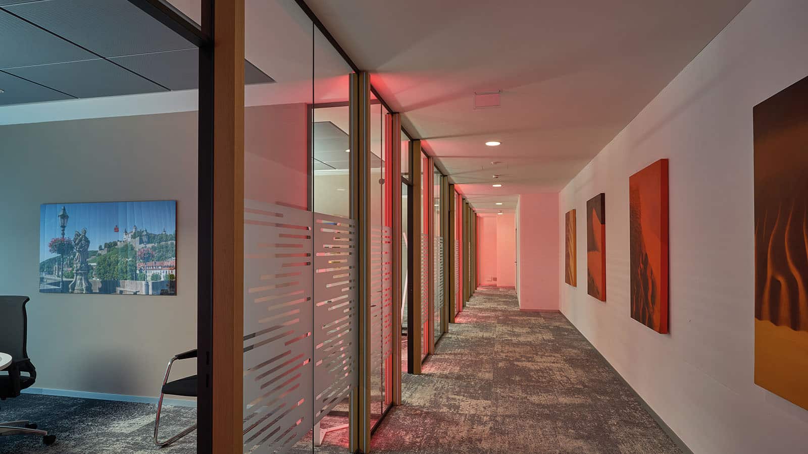 Bürokorridor mit roter Beleuchtung und Gemälden an Wänden.