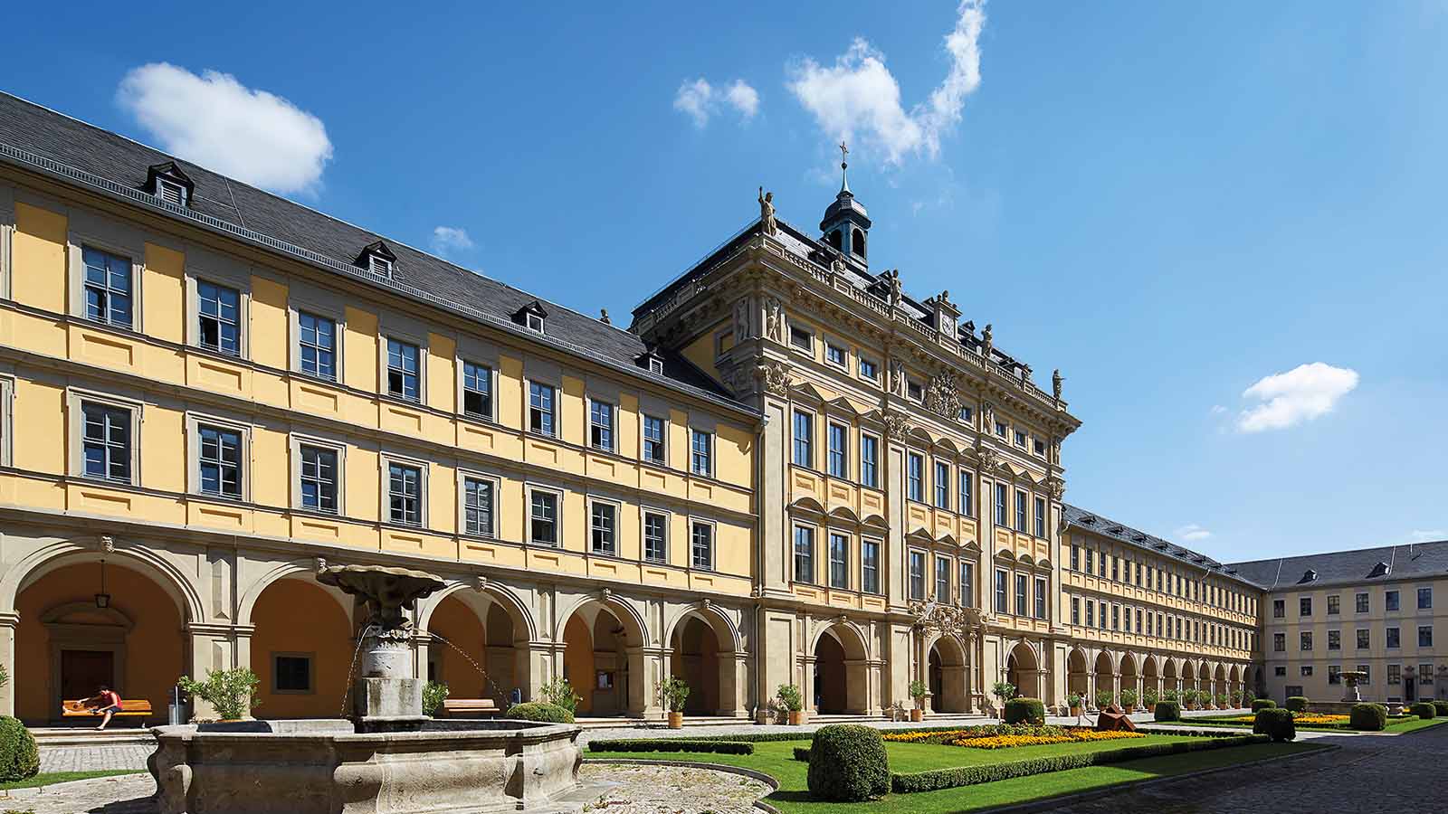 Historisches Gebäude mit Rundbogen und Brunnen im Innenhof.