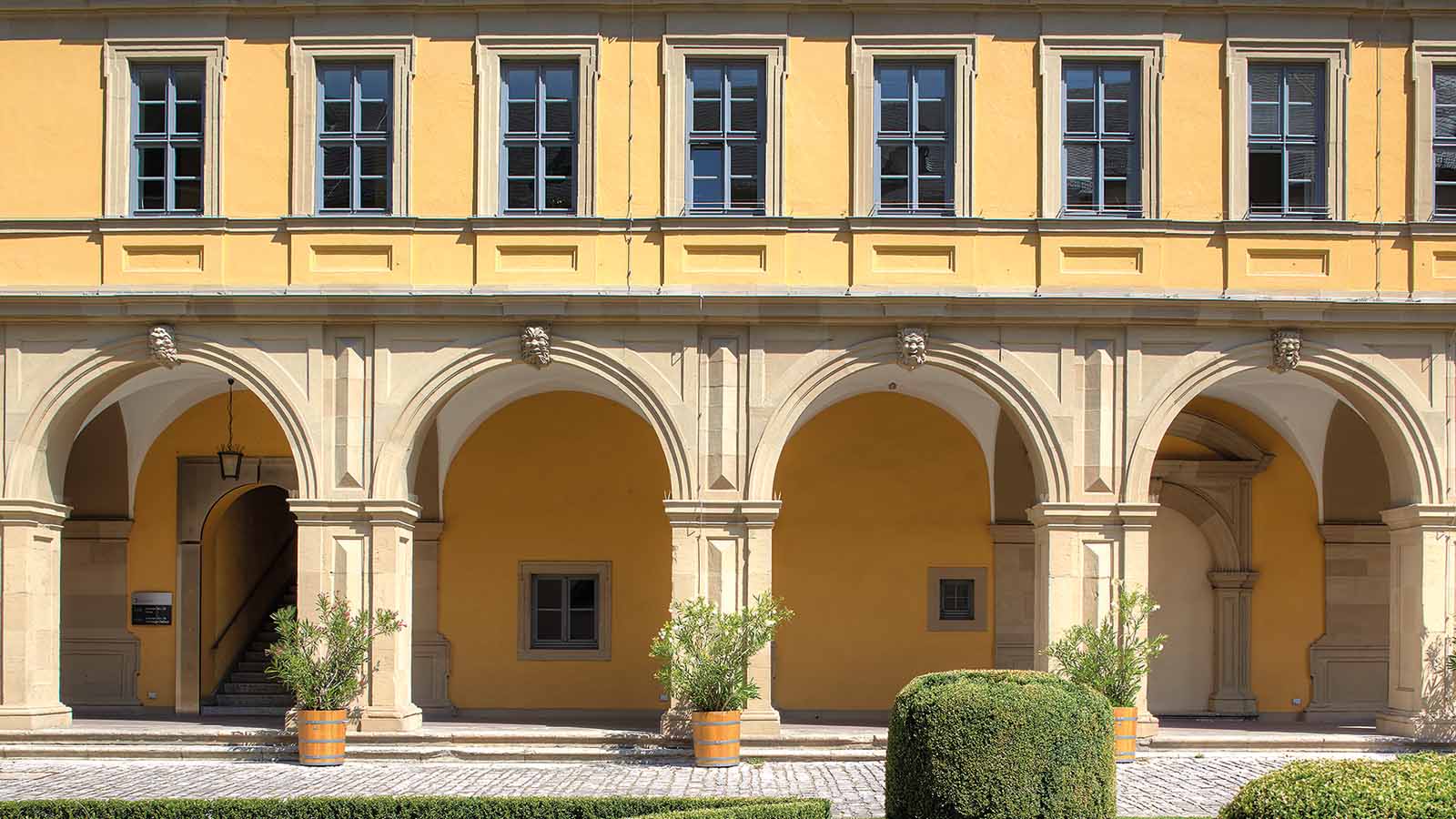 Historische gelbe Fassade mit Arkaden und Pflanzen.