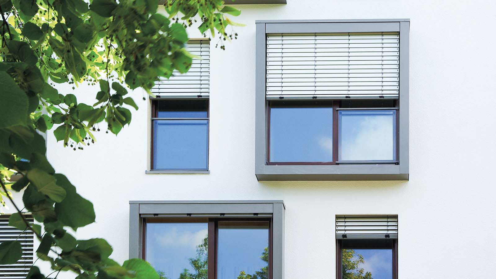 Moderne Fenster mit Rollos an weißer Hauswand