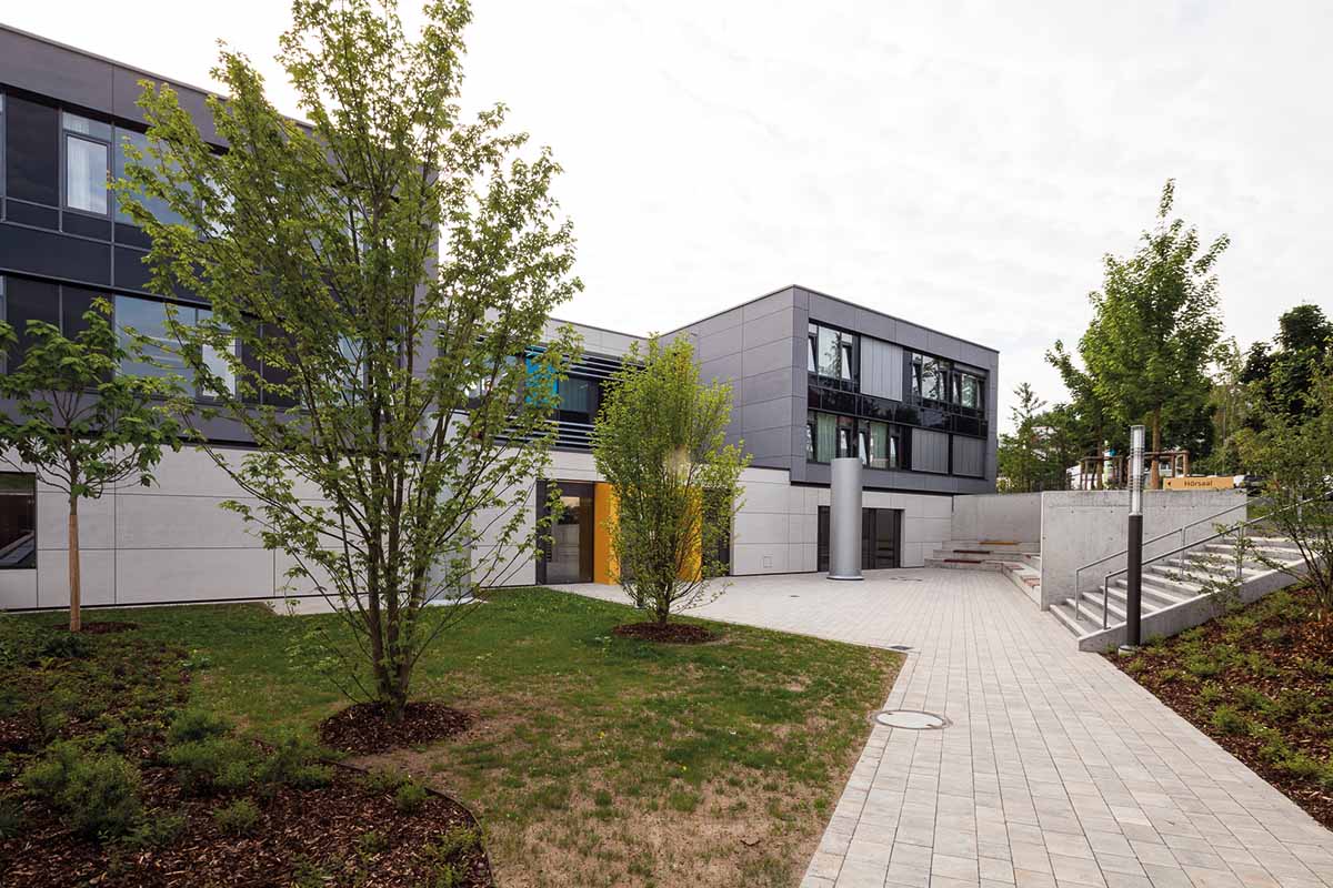 Moderner Bürogebäudehof mit Bäumen und Grünfläche.