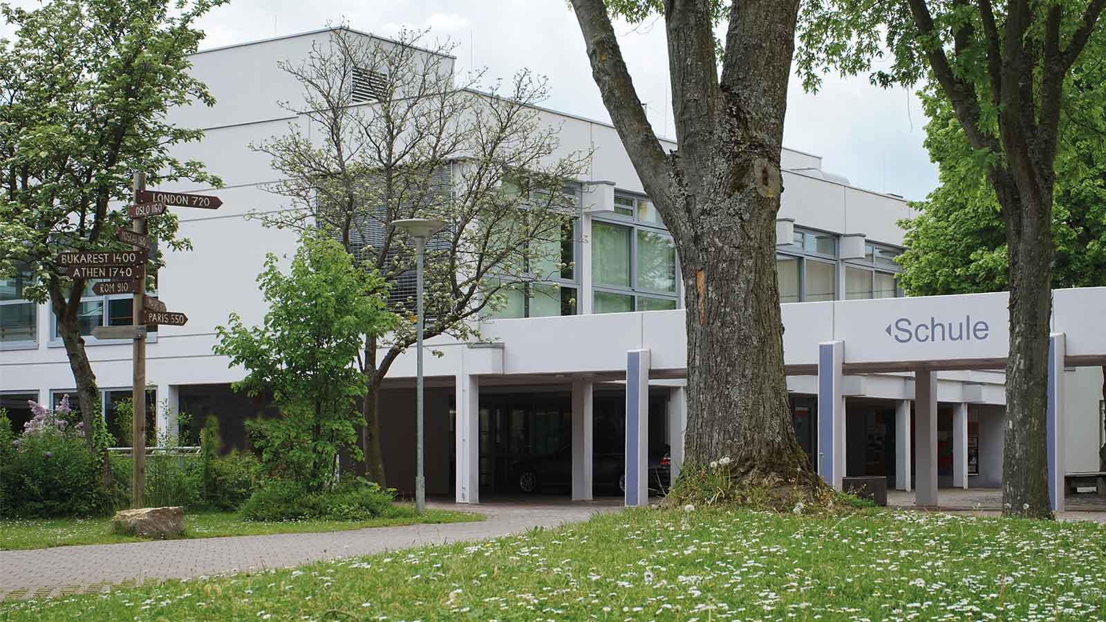 Schulgebäude mit Wegweisern im Vordergrund.