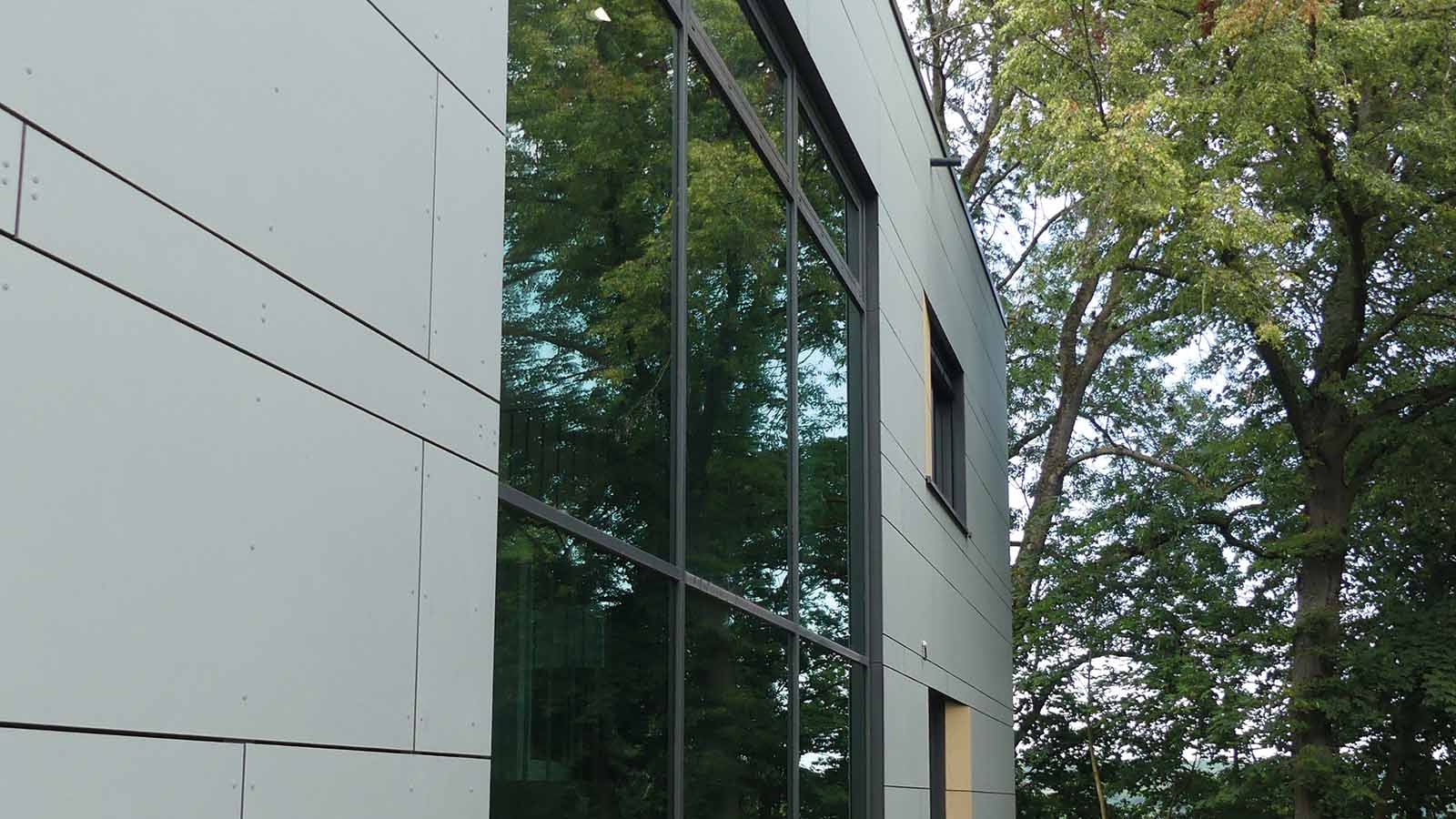 Moderne Glasfassade reflektiert umliegende Bäume und Himmel.