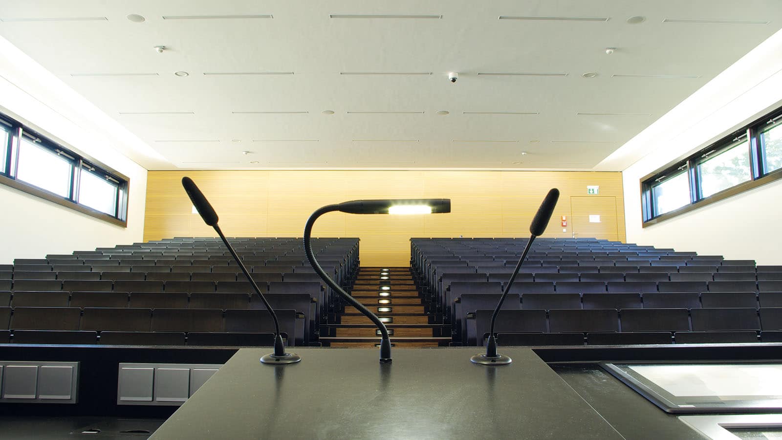 Leerer Hörsaal mit zwei Mikrofonen und Rednerpult.