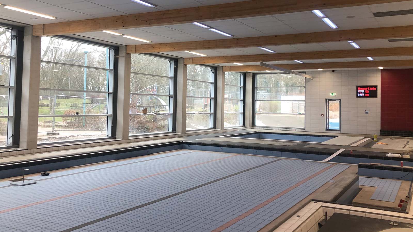 Leeres Hallenbad mit großen Fenstern und roten Wänden.