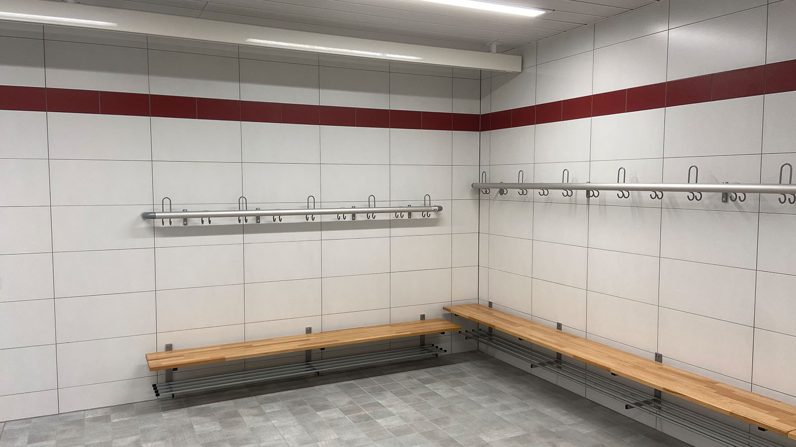 Leere Umkleidekabine mit Holzbänken und Haken.