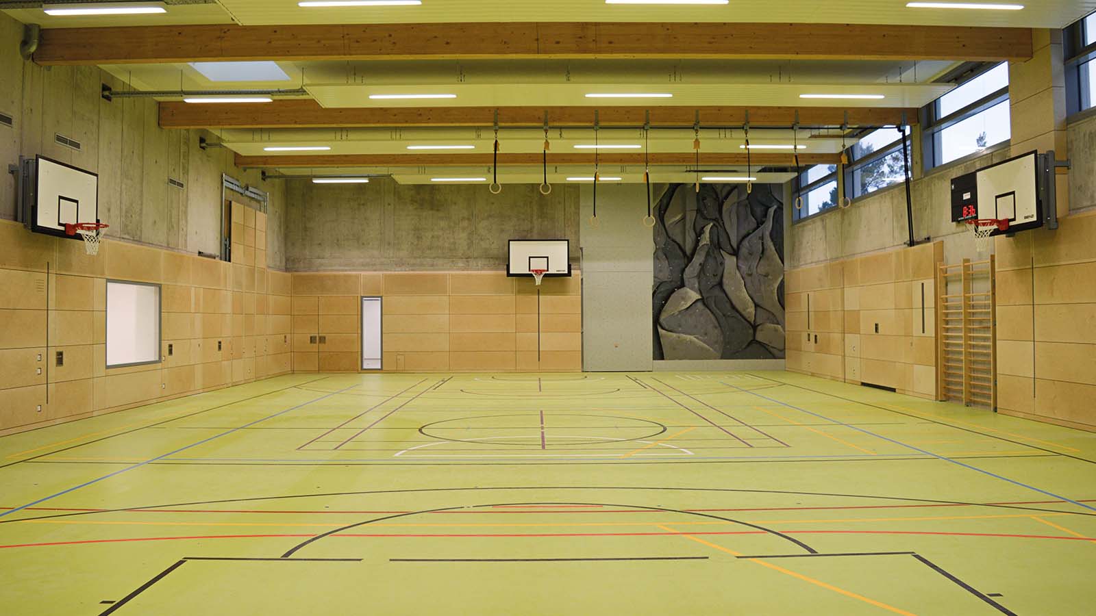 Leere Turnhalle mit Basketballkörben und Kletterwand
