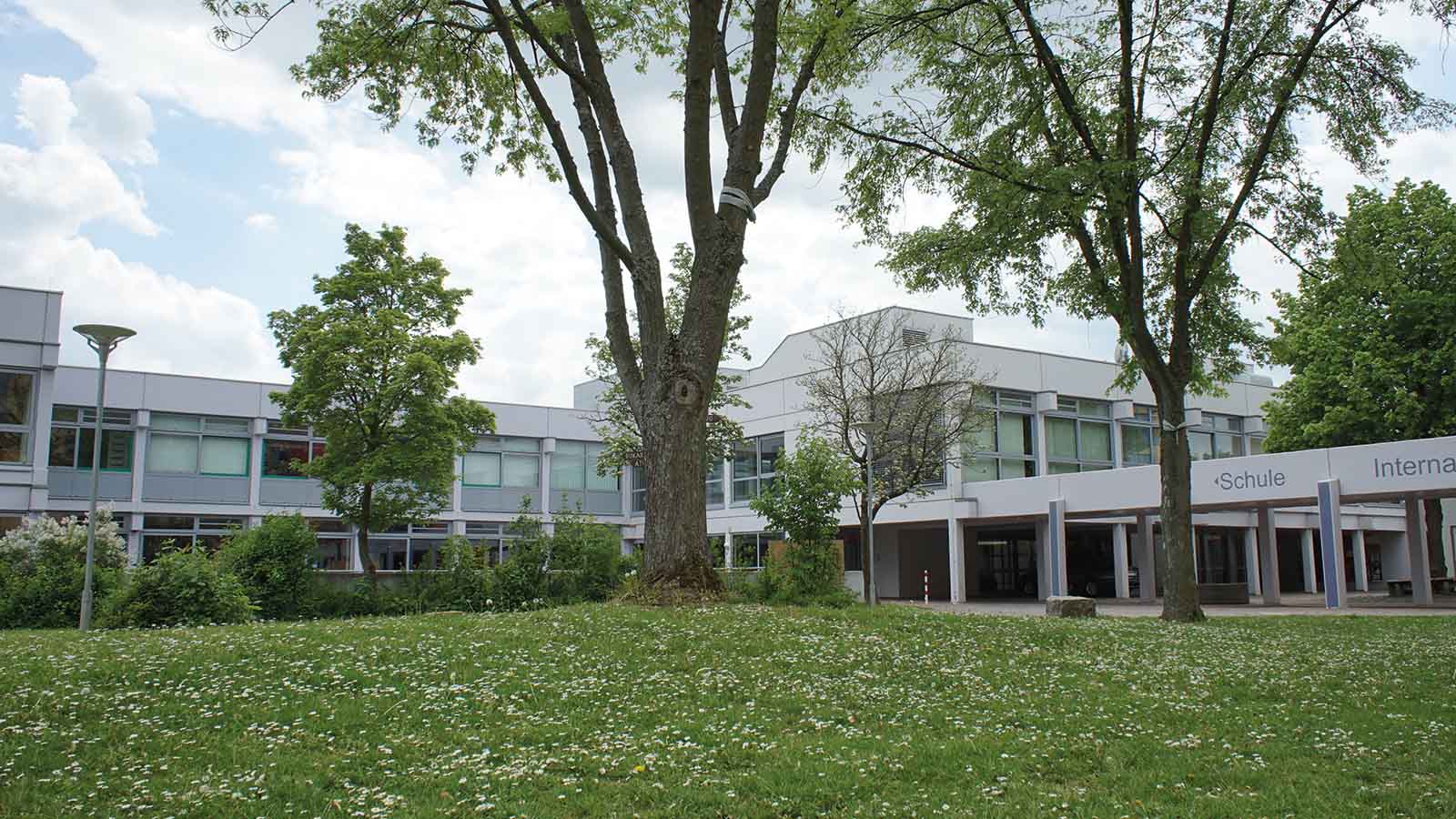 Schulgebäude mit Bäumen und Grünfläche im Vordergrund.