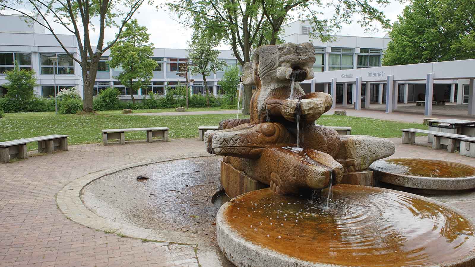 Schulhof mit Brunnen und Sitzbänken.