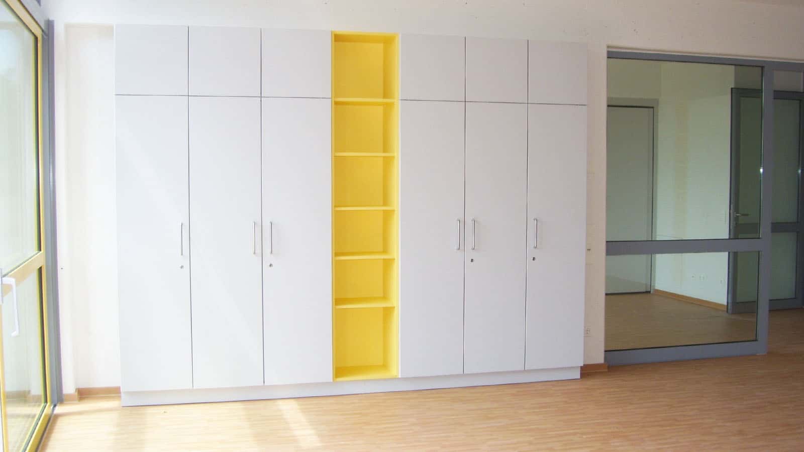 Weiße Schränke mit gelben Regalen in modernem Raum.