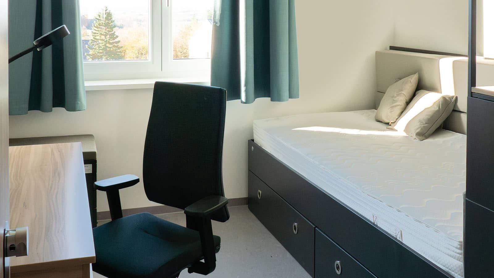 Modernes Studentenwohnheimzimmer mit Schreibtisch und Bett.