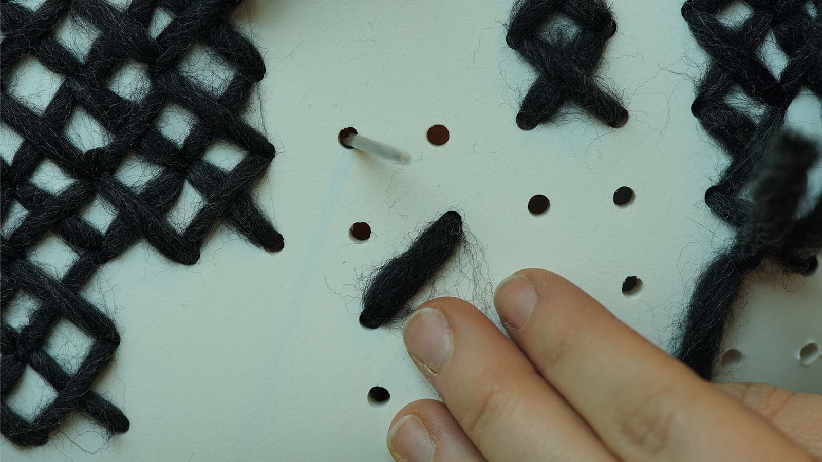 Hand webt schwarzes Garn auf Karton.